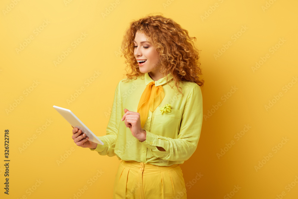 happy redhead girl looking at digital tablet on yellow happy redhead girl looking at digital tablet on yellow