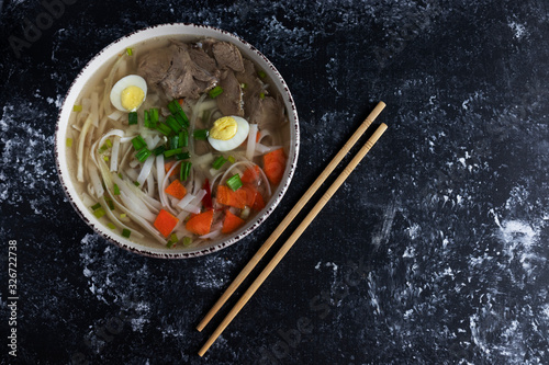 Flat lay, asian fo bo soup on black background with chives and carrots.