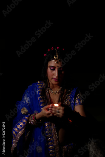 Young and beautiful Indian Gujarati woman in Indian traditional dress celebrating Diwali with illuminated diya/lamps on rooftop on Diwali evening. Indian lifestyle and Diwali celebration © abir
