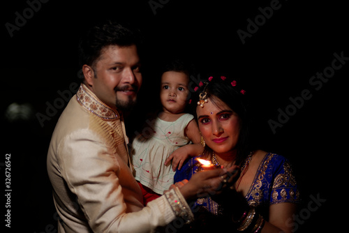 Young and beautiful Indian Gujarati father,mother and kid in traditional dress celebrating Diwali with diya/lamps on the terrace in darness on Diwali evening. Indian lifestyle and Diwali celebration