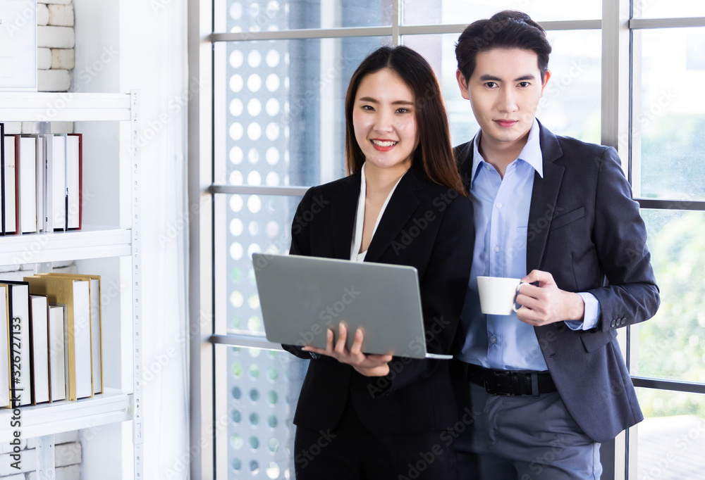 Young Asian businesswoman and businessman partners while working together with laptop computer and business man holding a cup of coffee in office background,Working couple Young Asian businesswoman and businessman partners while working together with laptop computer and business man holding a cup of coffee in office background,Working couple