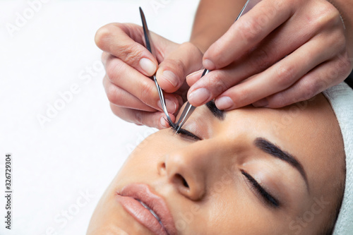 Cosmetologist doing the eyelash extension procedure on a woman over white background.