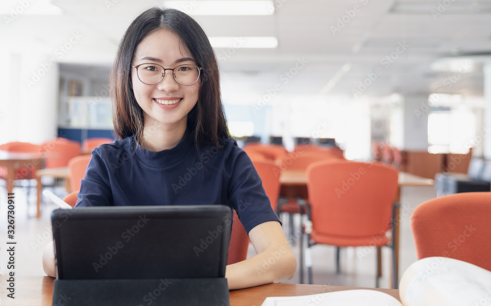 Back to school education knowledge college university concept, Beautiful female college student holding her tablet smiling happily sitting in library, Learning and education concept
