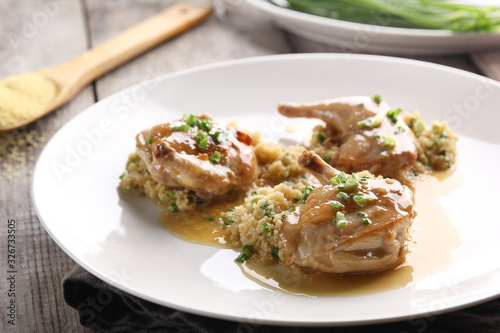 Grilled quail with couscous, sauce and green onions on a light wooden background. Background image, copy space