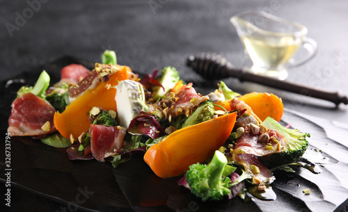 Salad with persimmon, cheese, broccoli and pistachios on a black background