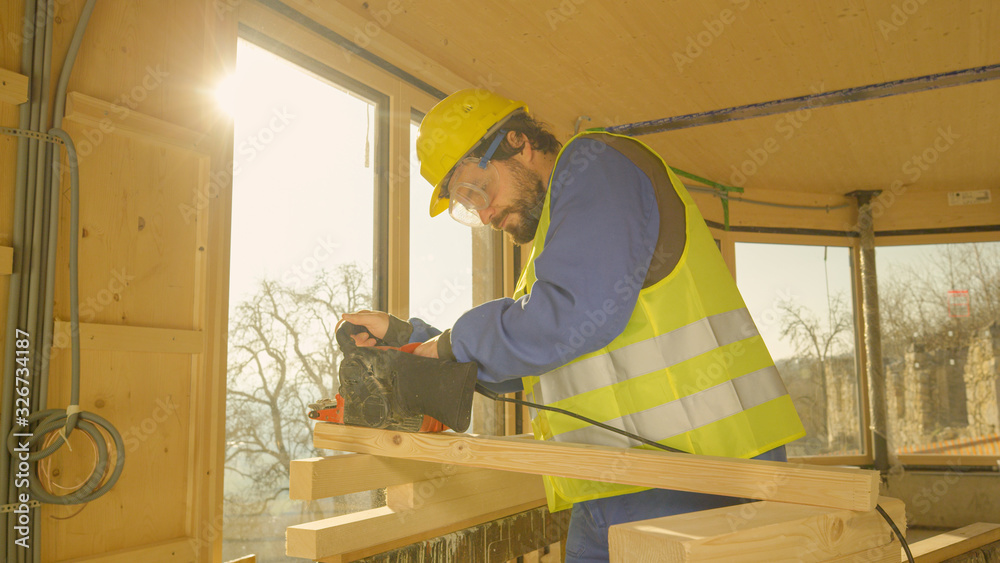 CLOSE UP: Young man working on a prefabricated house buffs a plank with a sander CLOSE UP: Young man working on a prefabricated house buffs a plank with a sander