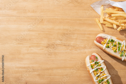 Fototapeta Naklejka Na Ścianę i Meble -  top view of delicious hot dogs with corn, green onion and mayonnaise near french fries on wooden table