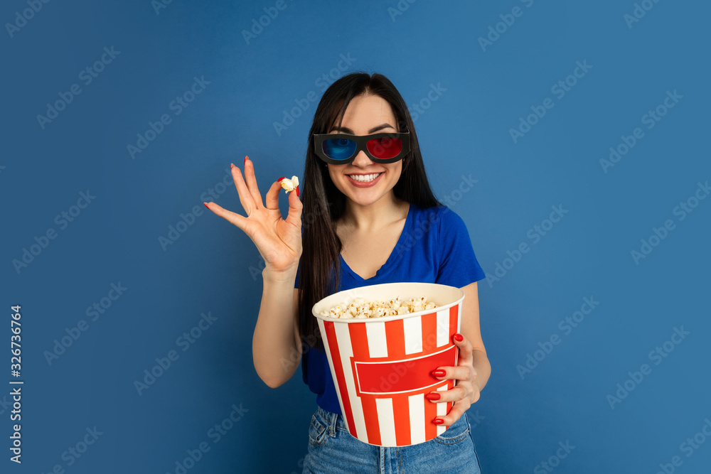 Obraz premium Emotional watching cinema. Beautiful caucasian woman's portrait on blue studio background. Beautiful female brunette model. Concept of human emotions, facial expression, sales, ad, copyspace.