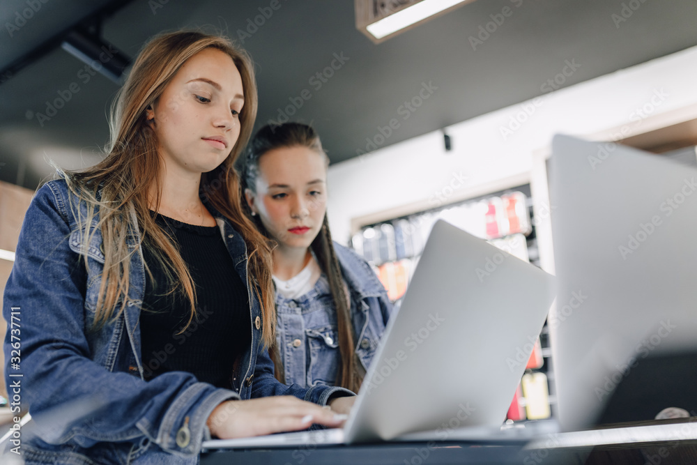 young attractive girls in an electronics store use a laptop at an exhibition. concept of buying gadgets. young attractive girls in an electronics store use a laptop at an exhibition. concept of buying gadgets.