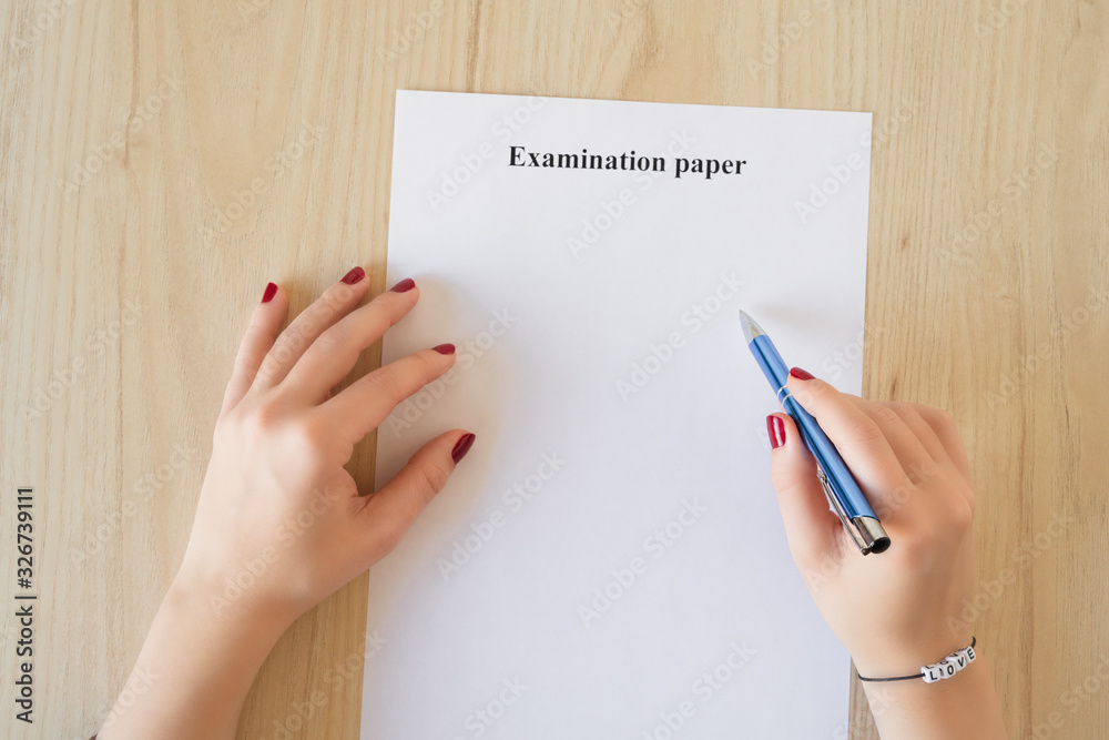 Student girl hand with bracelet and love word. Empty examination paper sheet on the table. First love during university exam. Concept Student girl hand with bracelet and love word. Empty examination paper sheet on the table. First love during university exam. Concept