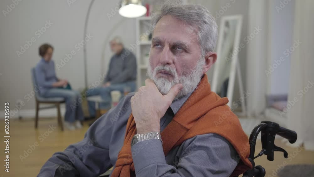 Senior graceful Caucasian man holding hand on chin and thinking. Portrait of aged retiree sitting in wheelchair in nursing home. Senior graceful Caucasian man holding hand on chin and thinking. Portrait of aged retiree sitting in wheelchair in nursing home.