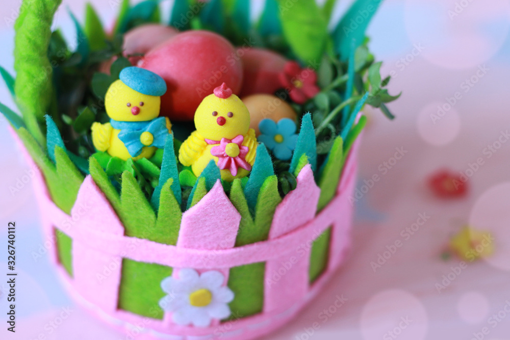 Fototapeta premium Bright colorful basket of felt with painted eggs and chicken on a pink-blue background. Handmade from felt. Happy Easter greeting card background pattern. Delicate pink and blue tones.