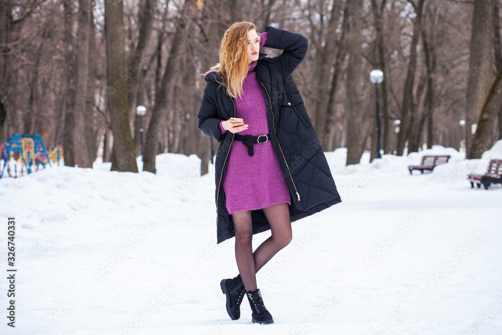 Full-length portrait of a young woman in black long down jacket posing in winter park