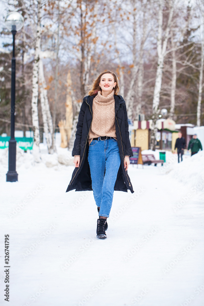Full-length portrait of a young woman in black long down jacket posing in winter park Full-length portrait of a young woman in black long down jacket posing in winter park