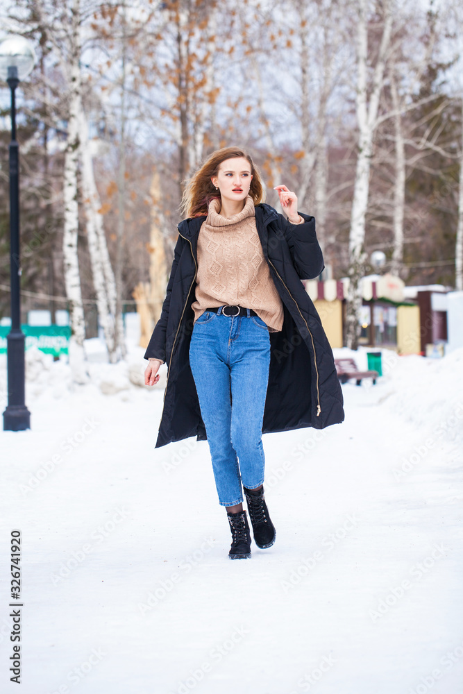 Full-length portrait of a young woman in black long down jacket posing in winter park Full-length portrait of a young woman in black long down jacket posing in winter park