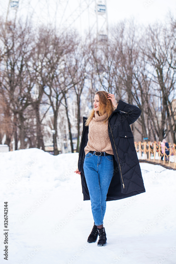 Full-length portrait of a young woman in black long down jacket posing in winter park Full-length portrait of a young woman in black long down jacket posing in winter park