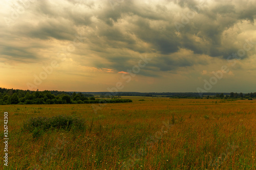 Picturesque clouds float over a wild meadow. The approaching storm. Ivanovo region, Russia.
