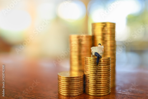 Money, Business, Saving and Planning concept. Close up of businessman miniature figure perople sitting and reading a newspaper on stack of gold coins on wooden table with copy space. photo