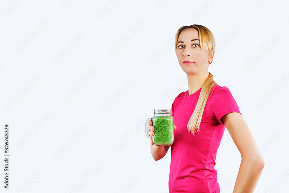 Sport blond girl in tracksuit for sport exercises with glass of green smoothie Sport blond girl in tracksuit for sport exercises with glass of green smoothie