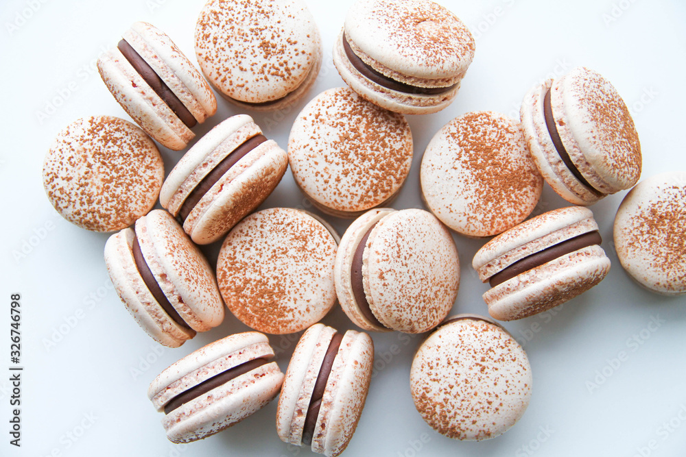 French dessert macaron powered with cocoa powder and filled with dark chocolate ganache. On a white background. Top view. French dessert macaron powered with cocoa powder and filled with dark chocolate ganache. On a white background. Top view.