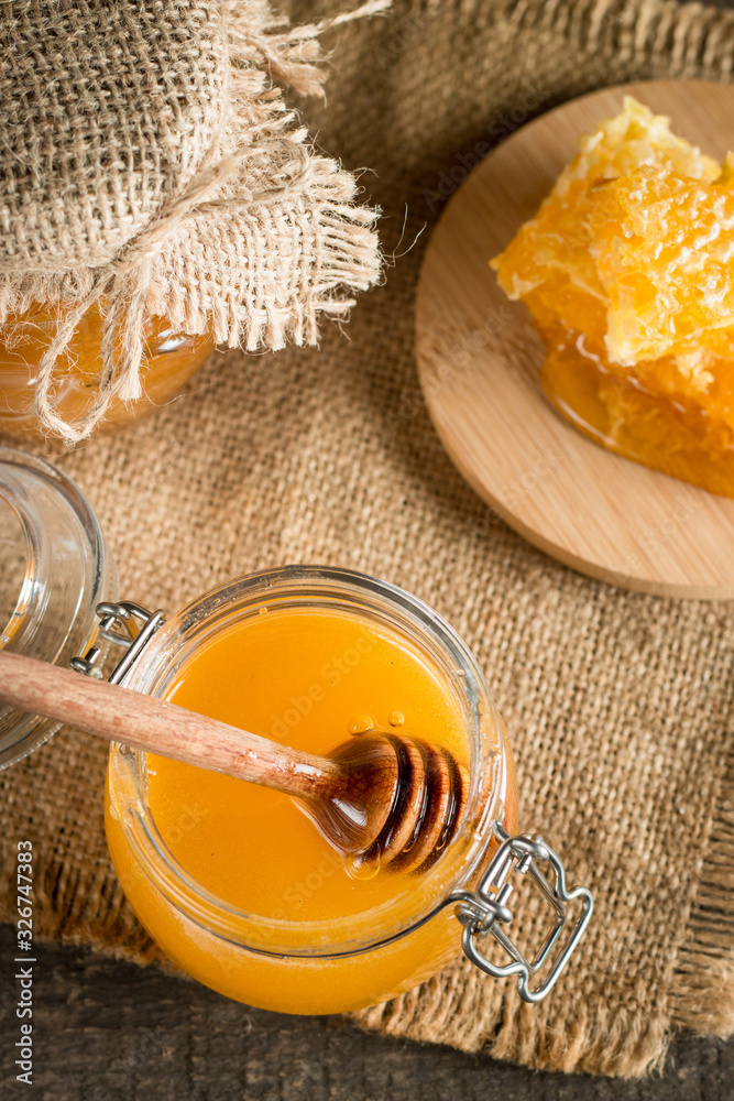 Honey dripping from a wooden honey dipper in a jar on wooden grey rustic background Honey dripping from a wooden honey dipper in a jar on wooden grey rustic background