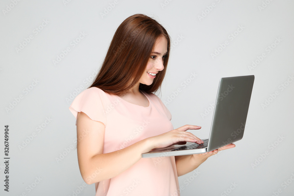 Young woman using laptop computer on grey background Young woman using laptop computer on grey background
