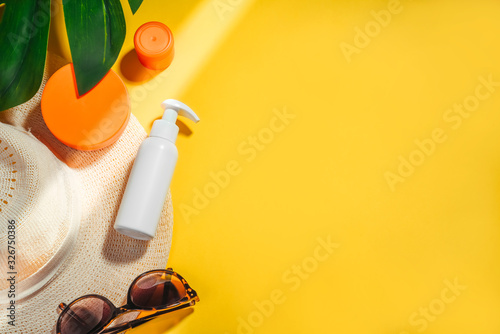 Sunscreen. Woman's hat with sunglasses and protection cream spf Flat lay on yellow background. Beach accessories. Summer Travel Vacation Concept photo