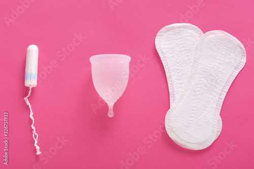 Horizontal flat lay of different types of feminine hygiene products, being isolated over pink background. Tampon, menstrual cup and hygiene pads, choice for women. Menstruation and women concept.