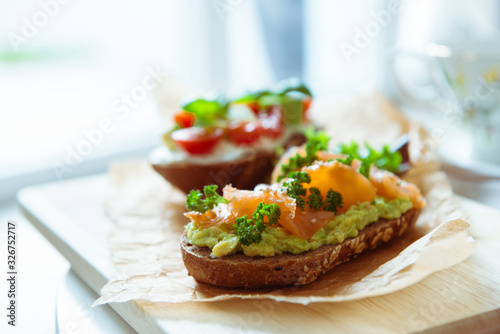 Wholegrain toast with avocado, tomato and salmon on wooden cutting board