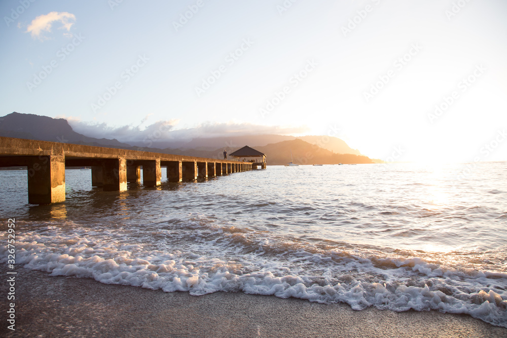 Beautiful pier extending into the sea during a golden Hawaiian Sunset.  Small waves and clear sky