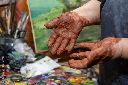 dirty hands in brown clay after sculpting on potter wheel against background of paint brushes