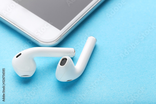 White wireless earphones with mobile phone on blue background