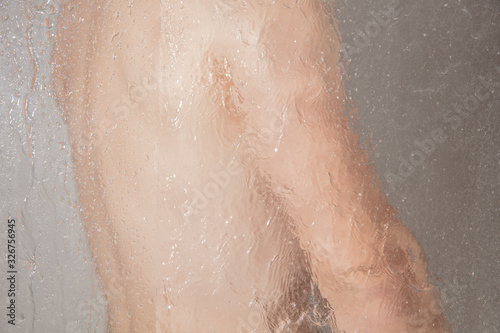 Männlicher Oberkörper hinter Duschwand mit Wasser