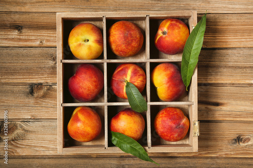 Fresh peaches with green leafs in crate on brown wooden table