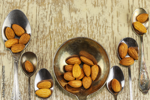 Metal spoons with almonds on a light wooden surface