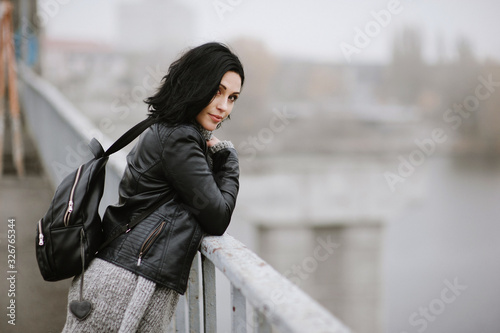 Side view of a young beautiful woman standing on the bridge and enjoing her life, urban lifestyle. Soft focus.