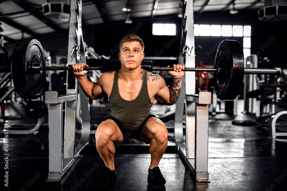Fit young man do squats with weights at the gym