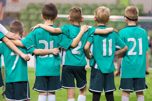 Team of young successful football players in spirts jersey uniform standing in row on field at the stadium. Kids in sports school team. Elementary age boys in football team.