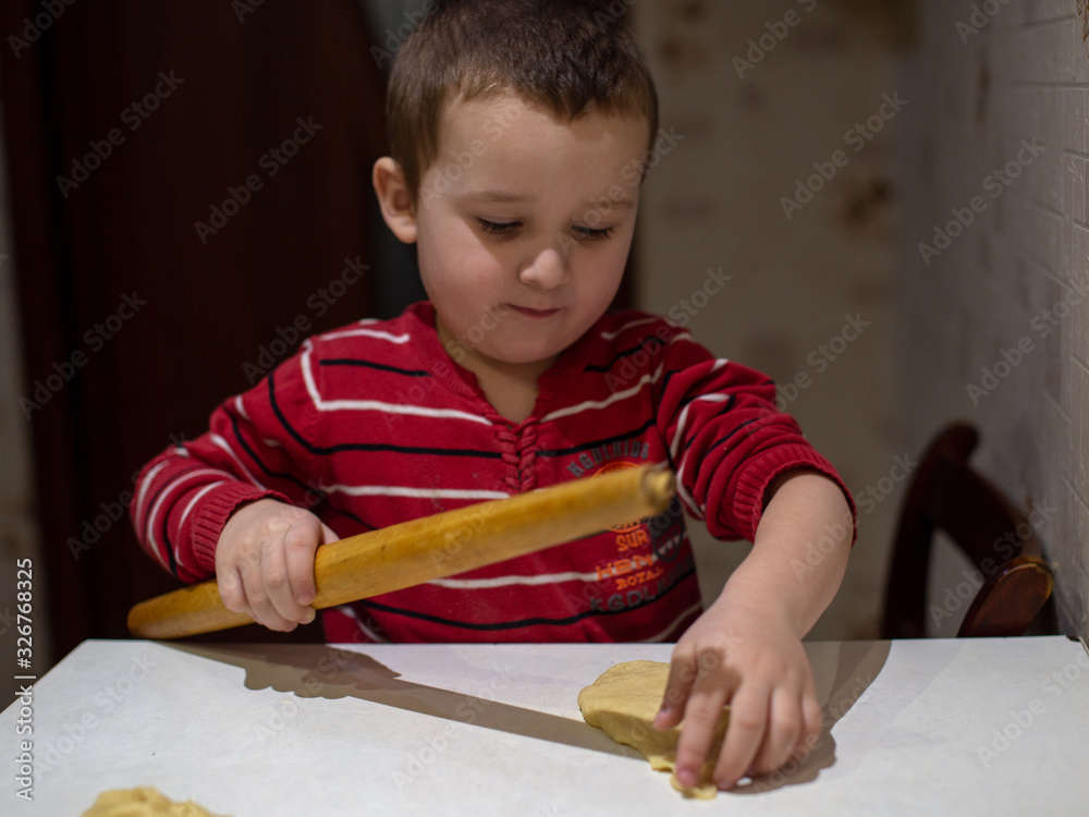 Little boy learns to cook pastries and helps parents. The boy holds a rolling pin in his hands. Little boy learns to cook pastries and helps parents. The boy holds a rolling pin in his hands.