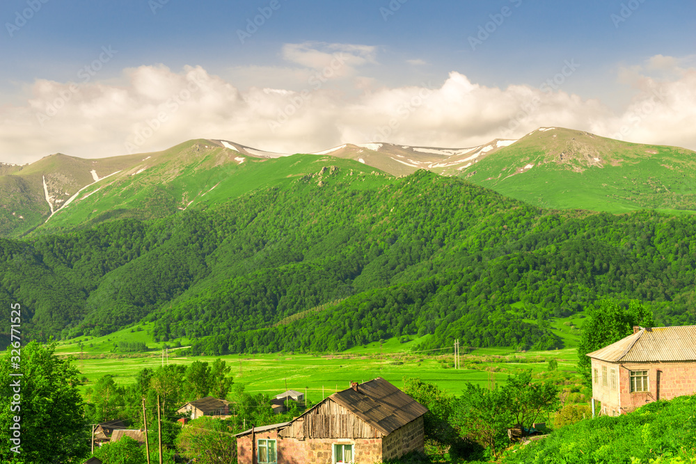 Mountain peaks covered with snow and green meadows on a sunny day in Armenia