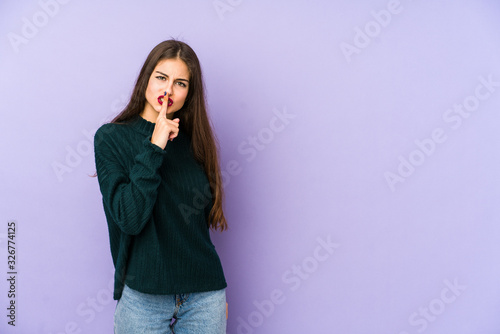 Young caucasian woman isolated on purple background keeping a secret or asking for silence. © Asier
