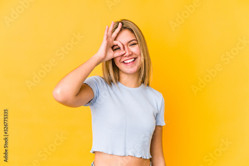 Young blonde caucasian woman isolated excited keeping ok gesture on eye.