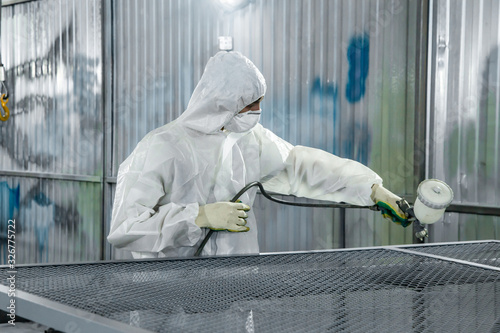 A paint shop worker with industrial sprayers in his hands.
