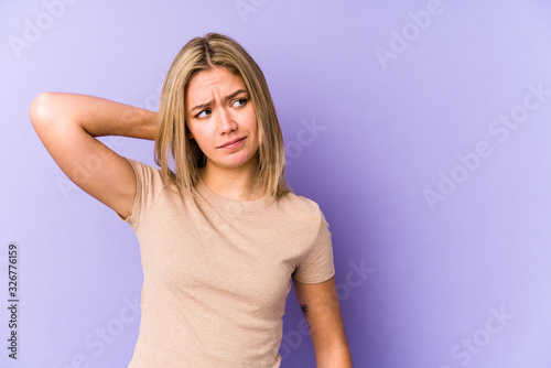 Young blonde caucasian woman isolated touching back of head, thinking and making a choice.