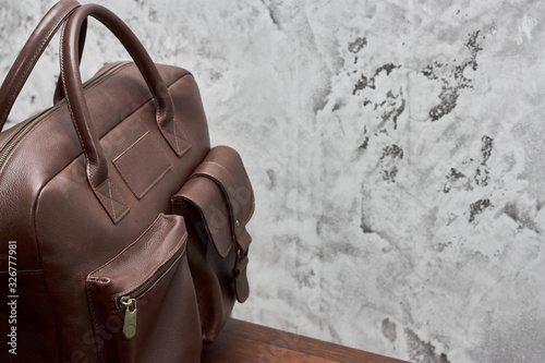 Leather business bag and accessories in the work room with gray concrete wall, wood table and leather chair.