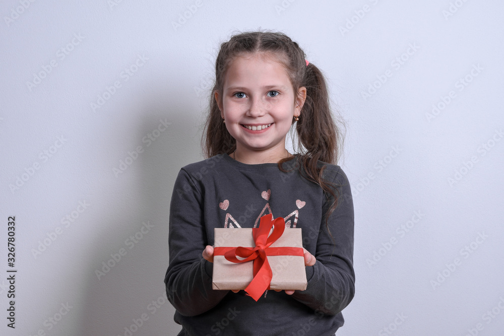 Portrait of a little white girl shows extends the gift on a gray background Portrait of a little white girl shows extends the gift on a gray background