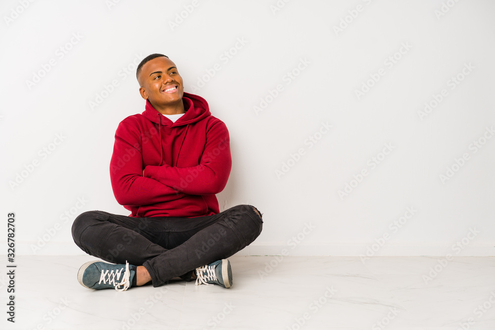 Young latin man sitting on the floor isolated smiling confident with crossed arms.