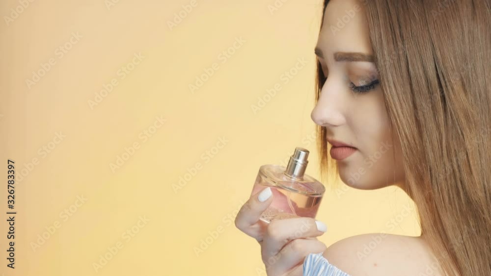 beautiful girl on a colored studio background enjoying the aroma of perfume from a bottle, a young woman sniffs and poses, the concept of female behavior and seduction beautiful girl on a colored studio background enjoying the aroma of perfume from a bottle, a young woman sniffs and poses, the concept of female behavior and seduction