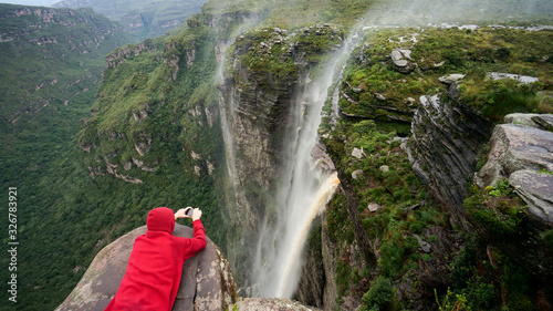 Traveler lies on the edge of the cliff and taking a picture of the waterfall in Chapada Diamantina national park, State of Bahia, Brazil.