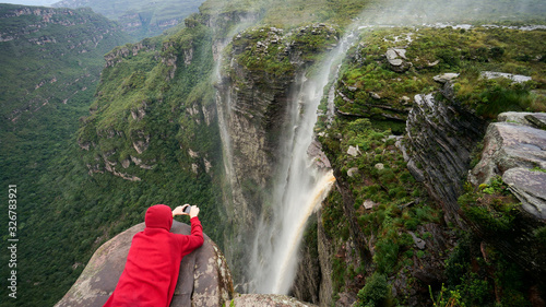 Traveler lies on the edge of the cliff and taking a picture of the waterfall in Chapada Diamantina national park, State of Bahia, Brazil. photo